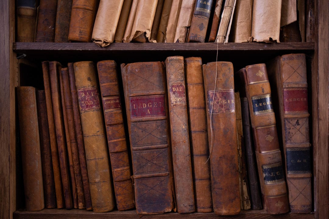 Old leather ledgers sit on a bookshelf