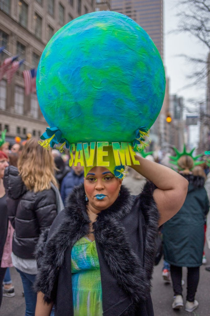 A woman wearing a hat shaped as Earth with letters spelling out "Save me"