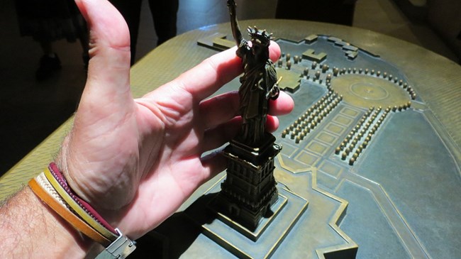 A hand touches a tactile display at the Statue of Liberty.