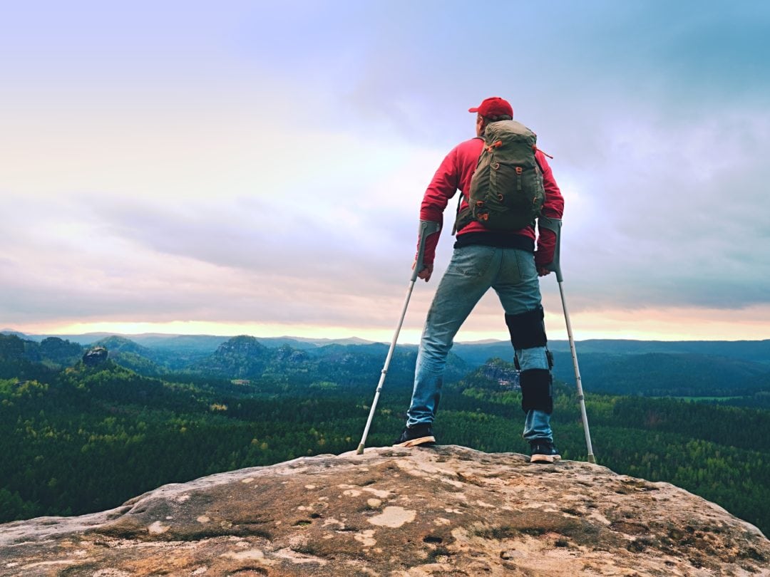 Man using crutches hikes a mountain