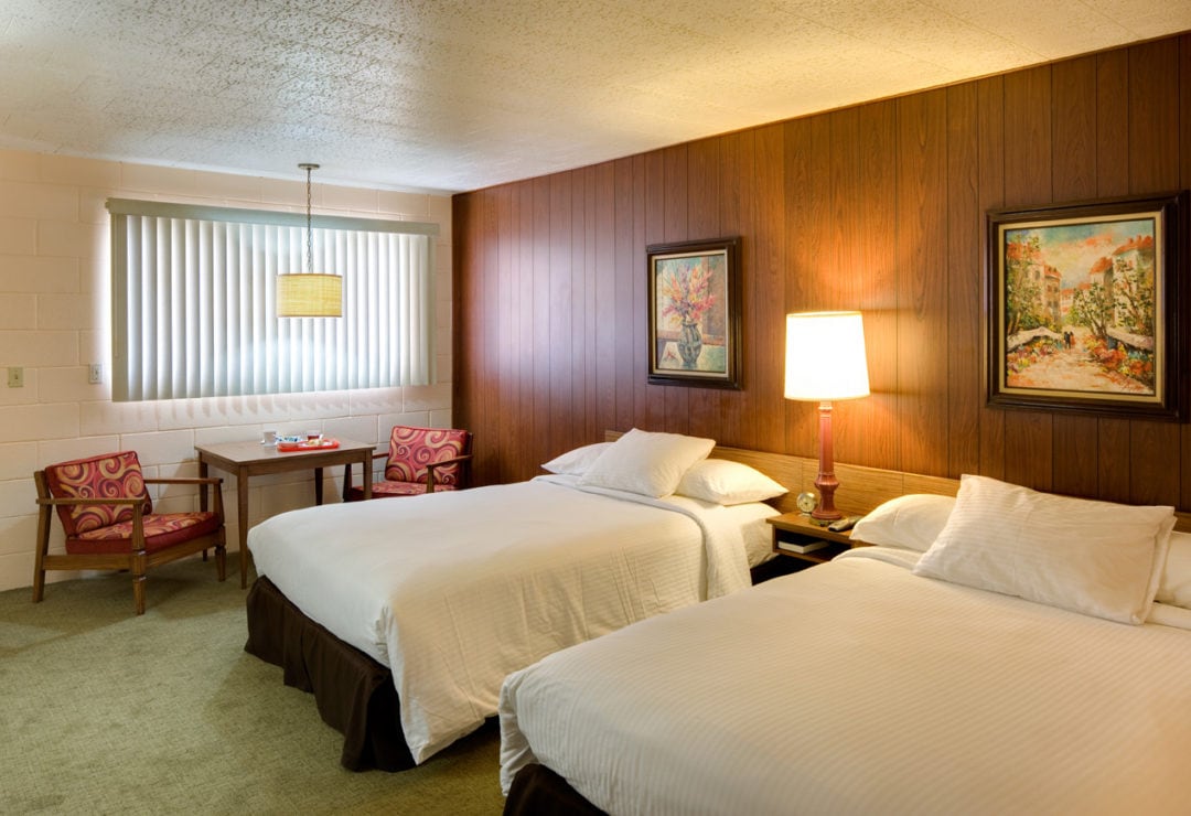A typical room at the Sunset Motel, with wood paneling, two full beds, and a lounge area.