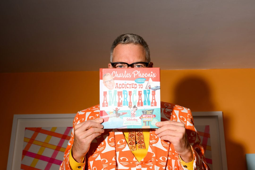 Charles Phoenix, in a bright orange cat-print suit, poses with his most recent book, 'Addicted to Americana.'