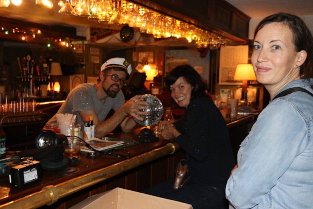 Three crew members from Alaska is a Drag pose with a disco ball in a bar.
