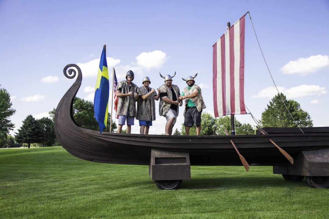 A group of men standing onboard a viking ship surrounded by a Swedish and an American flag in Columbia Township, Nebraska. 