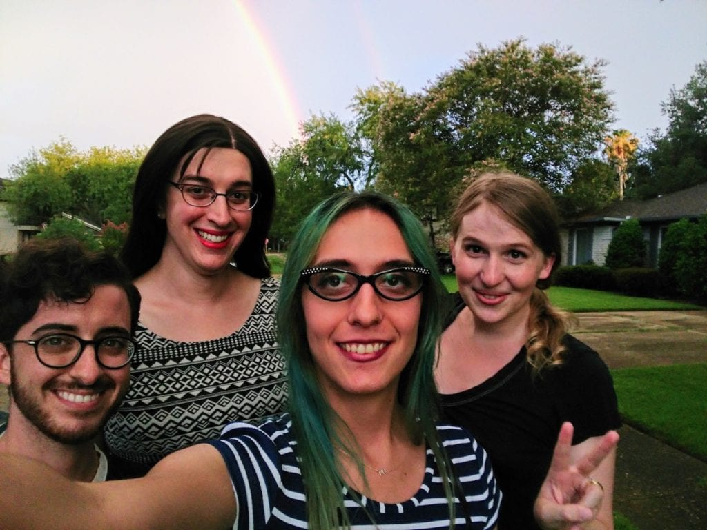 Four friends stand together under a rainbow.