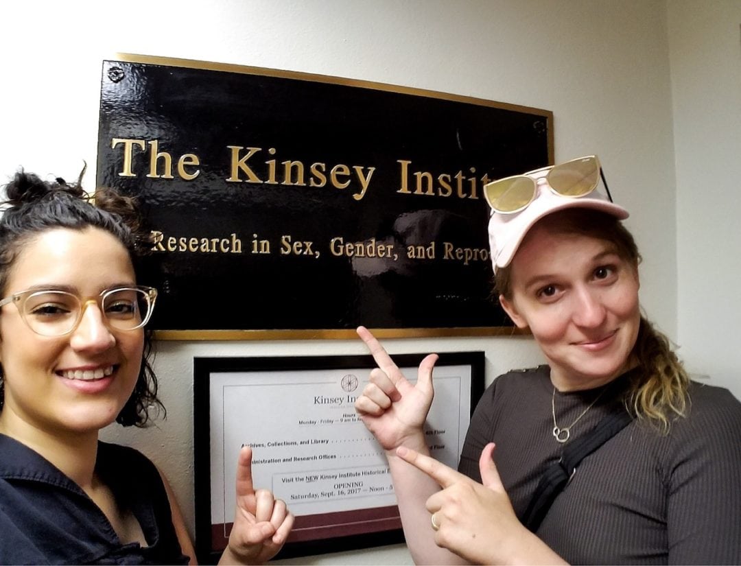 Corey and Samantha stand in front of a sign that reads, "The Kinsey Institute: Research in Sex, Gender, and Reproduction"