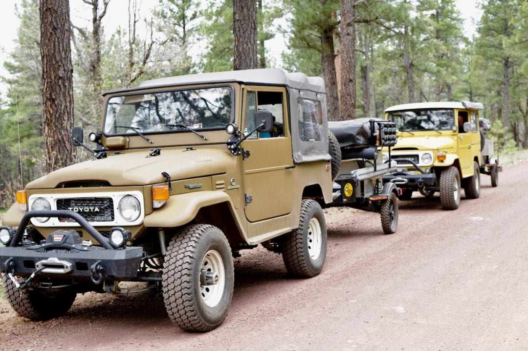Two 4x4 trucks parked along the roadside in a forest