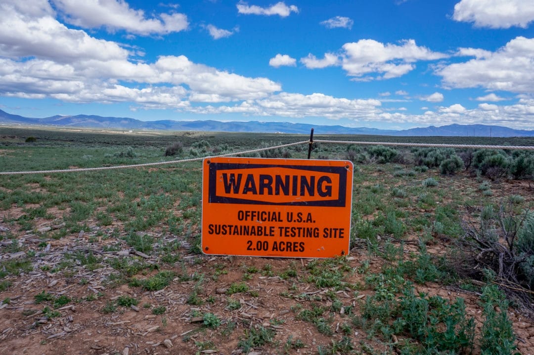 A bright warning sign reads: Warning. Official USA Sustainable Testing Site. 2.00 Acres. 