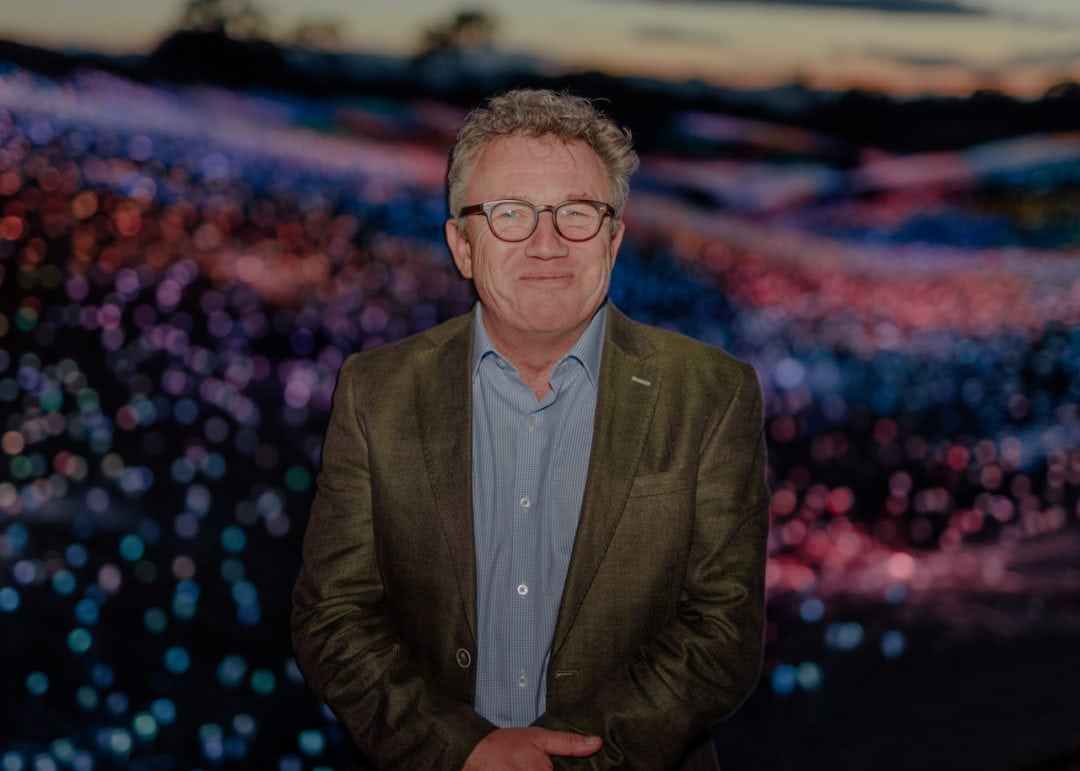 Bruce Munro stands in front of the illuminated field of lights