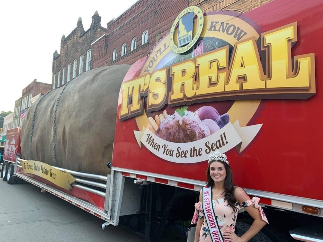 a girl in a flower dress and sache stands in front of the potato truck
