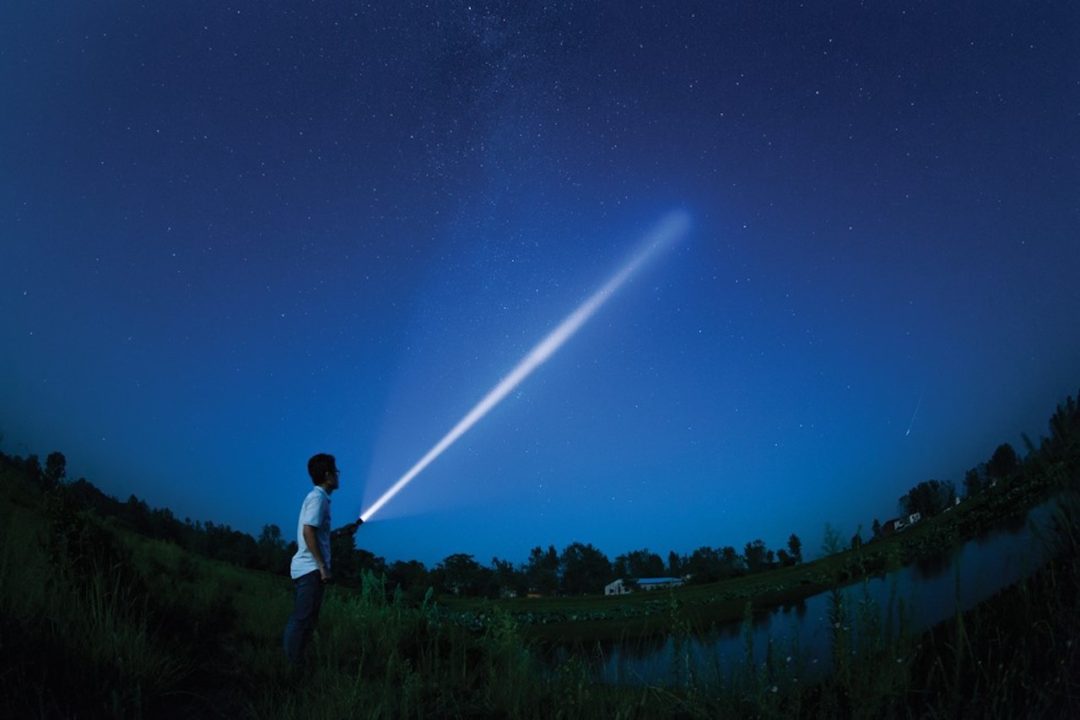 a guide with a flashlight points up at the night sky