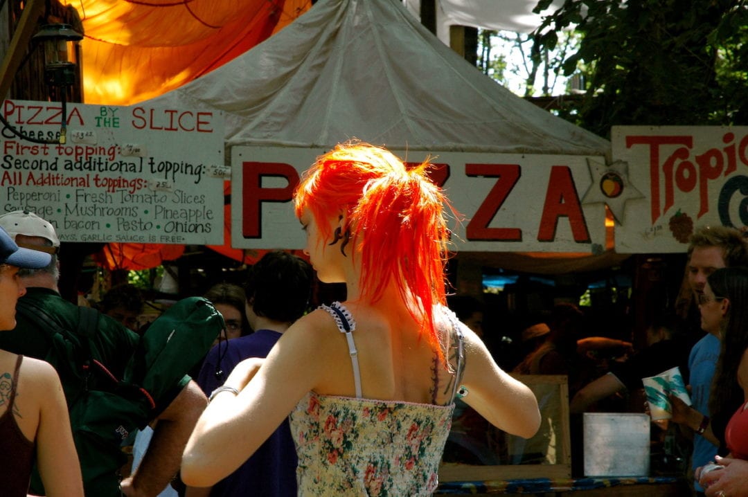A woman with bright red hair stands in line for pizza