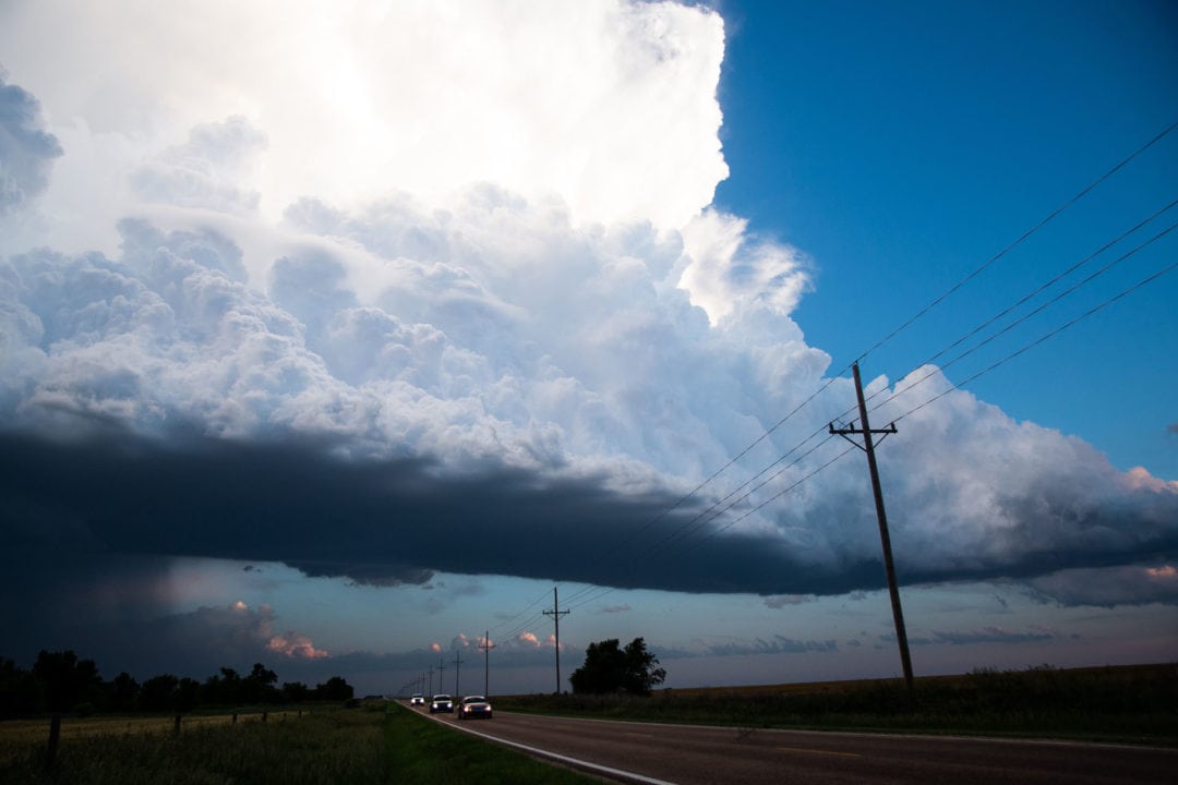 a supercell descends upon a grassy field and road