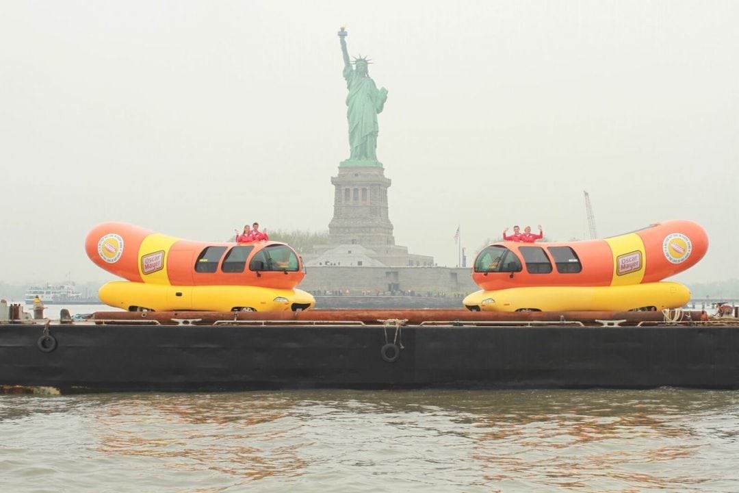 two wienermobiles in front of the statue of liberty on a barge
