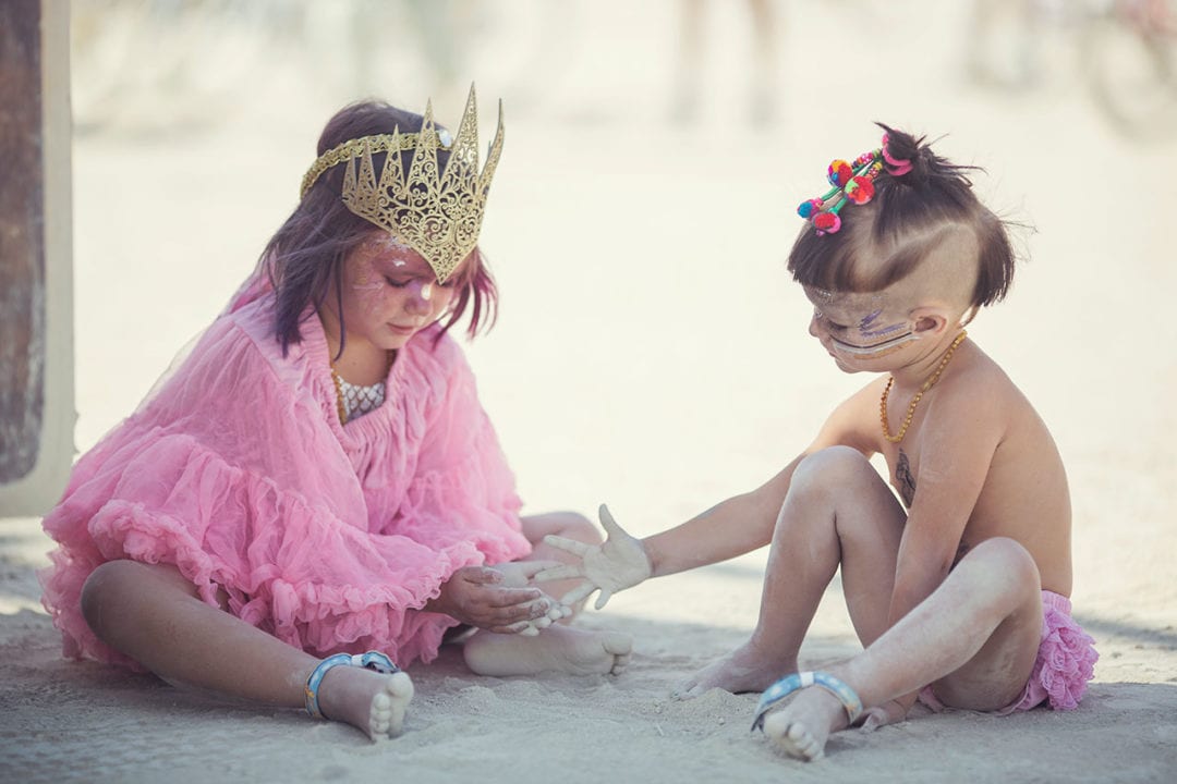 Two children dressed in colorful outfits play in the desert sand