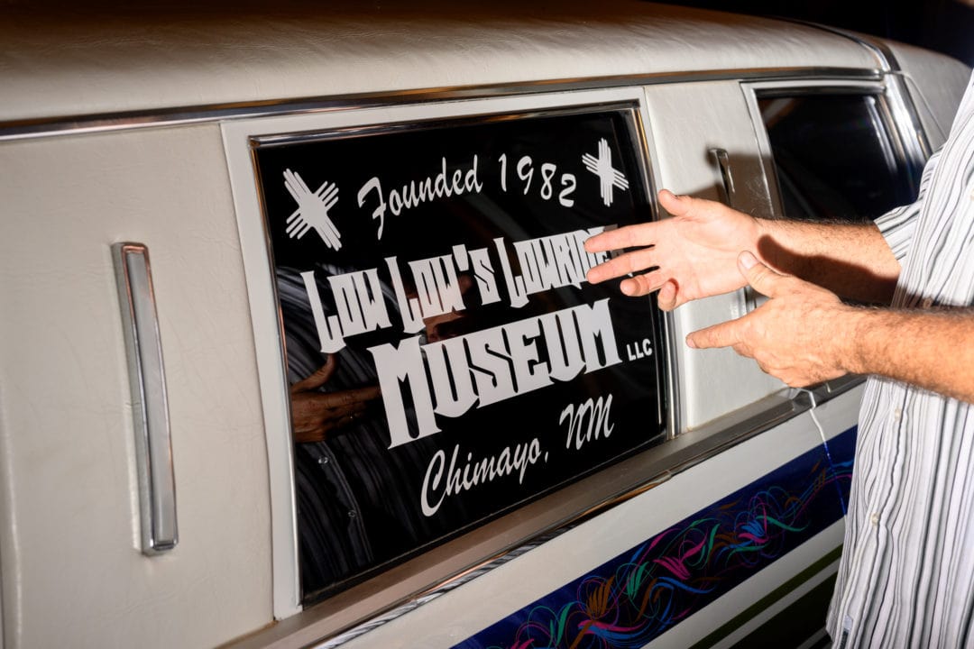 Window decal on the Chrysler, reading "Low Low's Lowrider Museum"