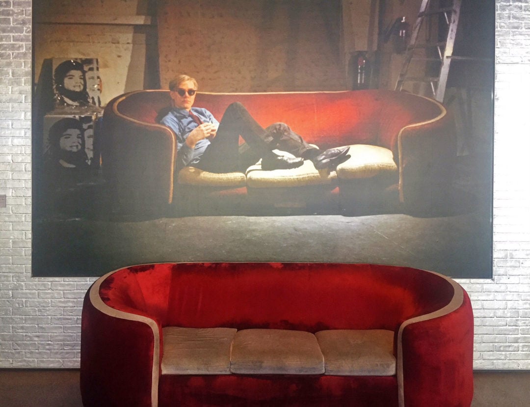 a red velvet couch with a photo hanging above it of the same couch with any warhol sitting on it