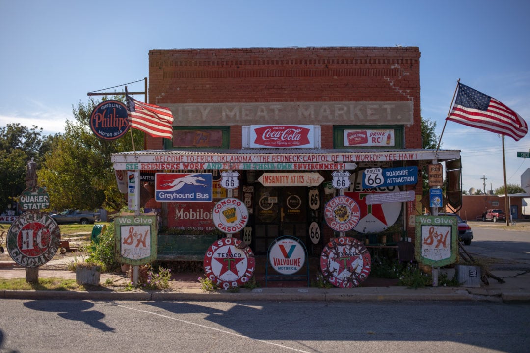 a small brick shop with flags, vintage auto signs and a painted sign that says "city meat market" on top