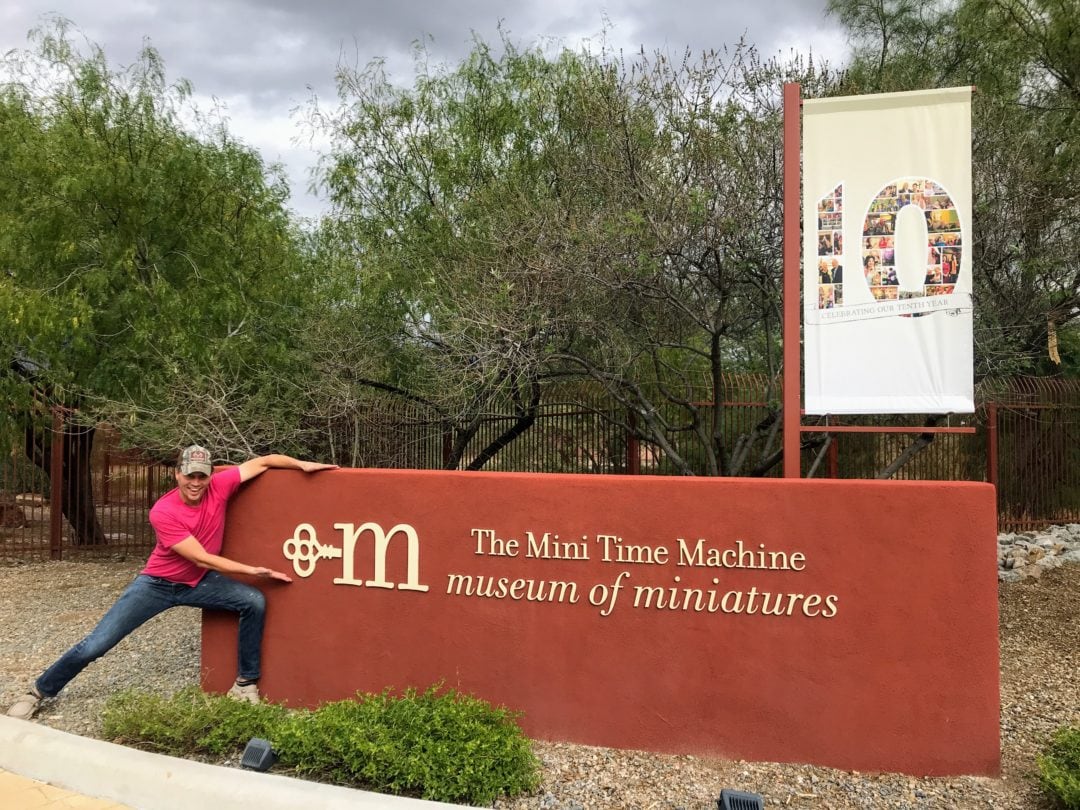 Josh posing in front of the red welcome sign at the Mini Time Machine Museum of Miniatures in Tucson, Arizona