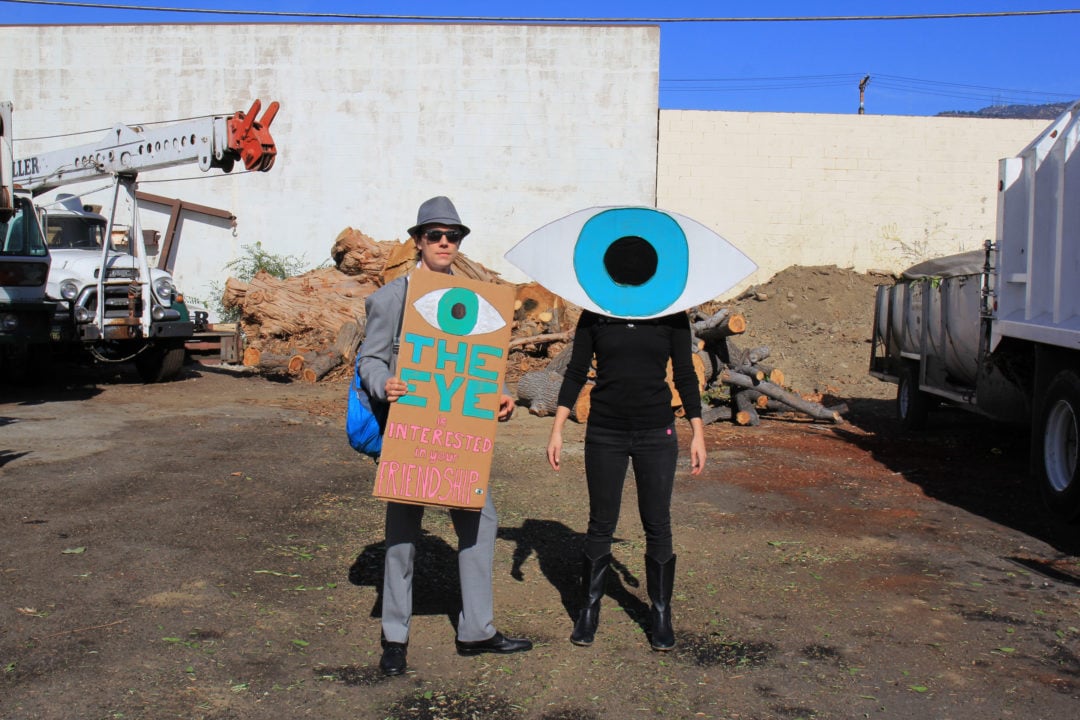 The Eye, and friend-of-the-eye Evan, makes a third visit to the Doo Dah Parade this year. Interested in your friendship, The Eye is a source of benevolent oddity and communicates to friends through prepared messages on signs carried in the parade. “You are visible,” The Eye says. “Tenderness is your strength.”