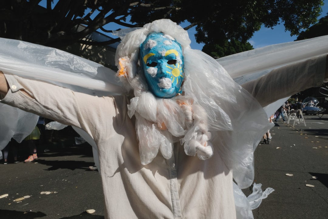 An environmental activist is dressed as a white and fluffy trash cloud made from disposable plastic grocery store shopping bags. Environmentalist awareness groups participate in the parade to protest consumerism and materialism. One such group puts on a trash fashion show to the Madonna song “Material Girl.” The “trashion” models made their garments entirely from garbage reminding us that our trash remains forever. They say that if we continue to consume items such as single-use plastics, we will be living on a future planet of trash.