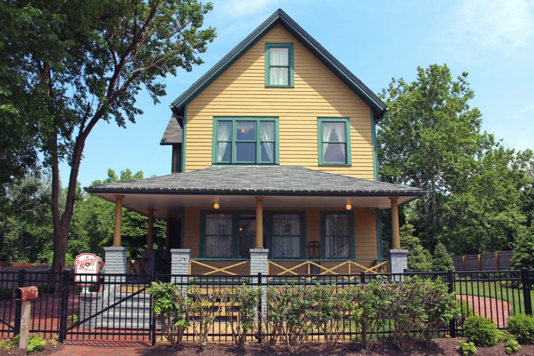 a yellow and green house with a porch and an black iron fence