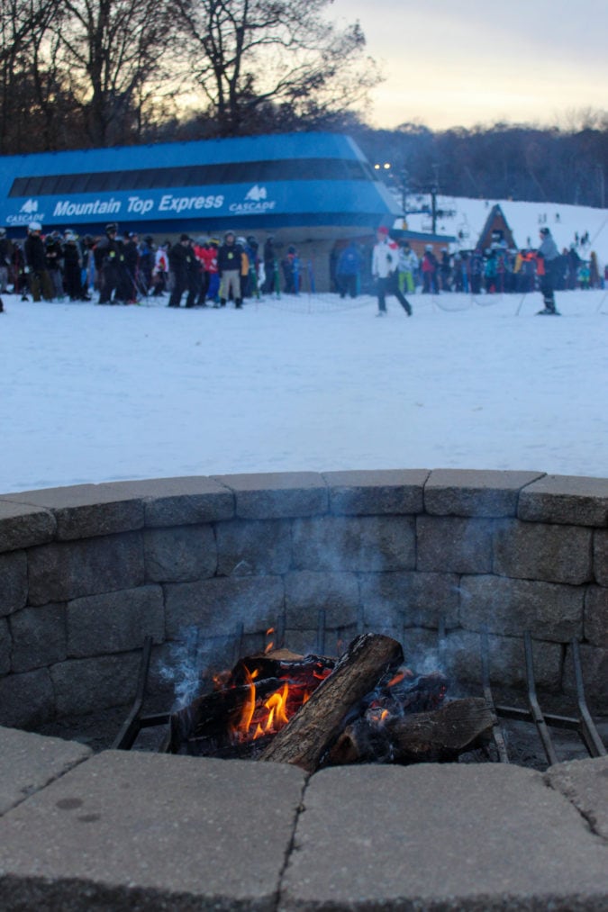 Fire pit at the base of ski hill, with ski lift line in the background