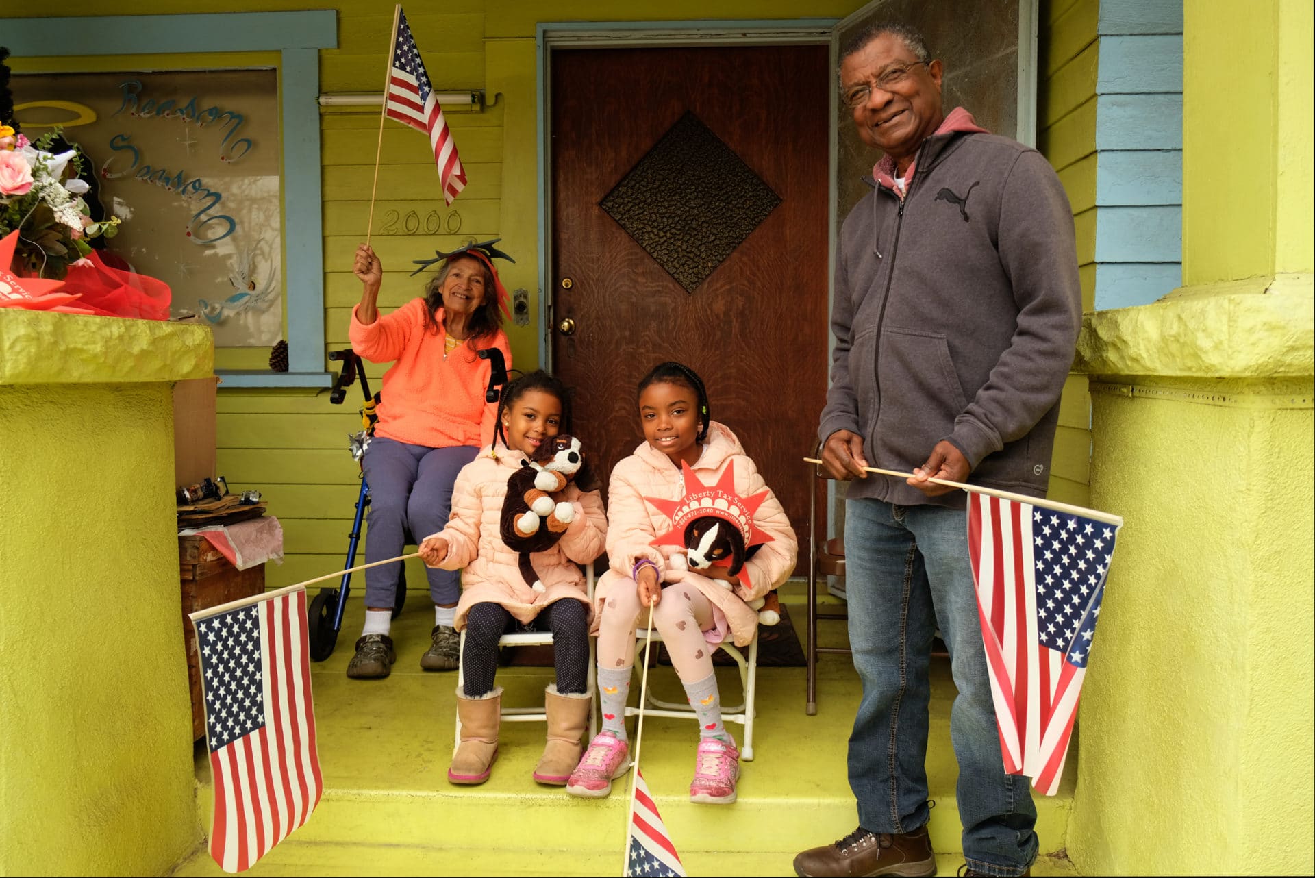 Sisters Isley and Manhattan are holding flags with their grandparents, Luz and Fabio Castillo. The Castillos have lived on Martin Luther King Jr. Boulevard for 43 years and have seen every parade from their porch since the start in 1985. The girls sit with their stuffed dogs, Spotty and Brownie, and say their favorite part of the parade is watching the horses.