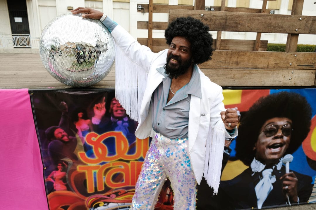 Marco De Santiago, one of the original Soul Train dancers, poses with a disco ball. De Santiago was on the popular television dance show from 1976 until 1993. He participates in the parade with other Soul Train alumni, dancing in vintage clothing and platform shoes to classic soul and R&B songs.