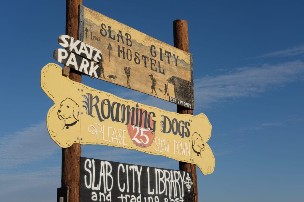 Signs at the entrance of Slab City advertise the local hostel and library.