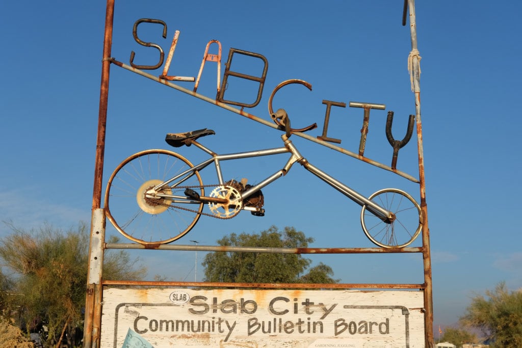 A community bulletin board features Slab City news and information.