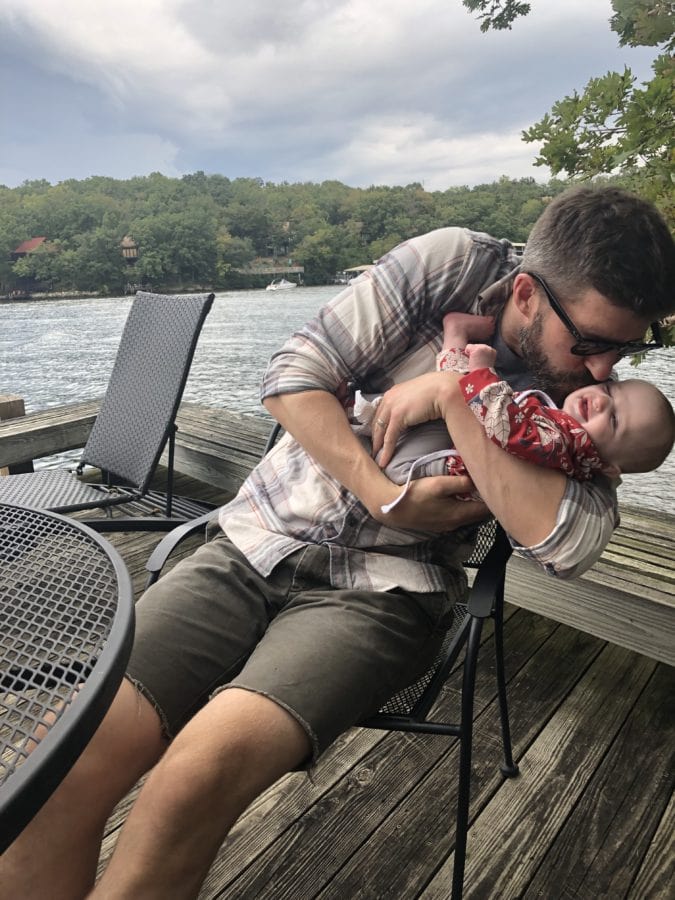 Dad sitting on a dock hugging and kissing his baby daughter