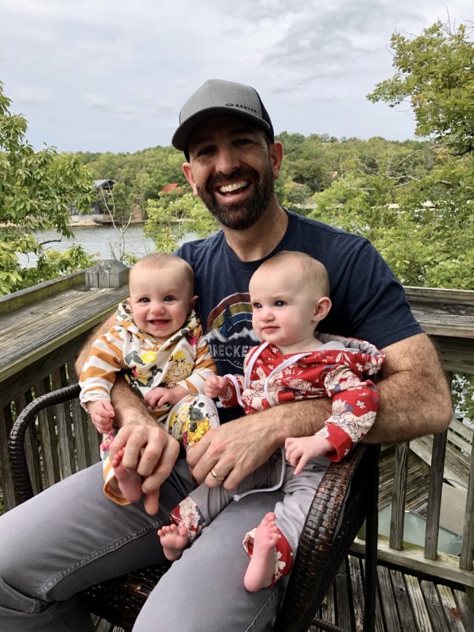 Smiling dad sitting on a deck holding twin baby girls