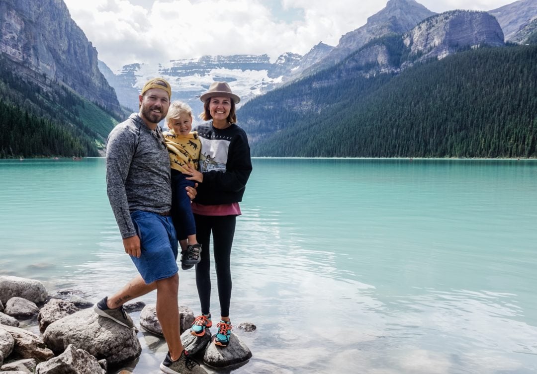 Father and mother told a little boy together and stand in front of a crystal blue lake in Banff National Park