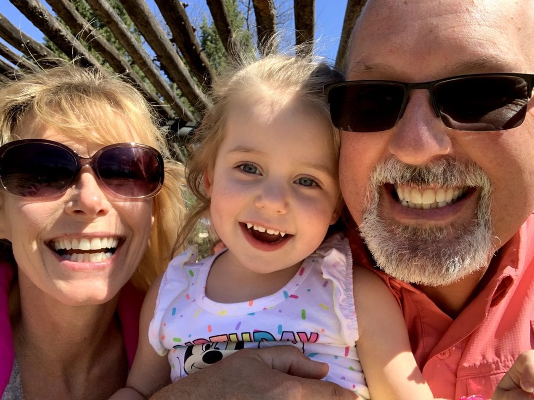 Selfie of a young grandmother and grandfather in sunglasses holding and smiling with their young granddaughter