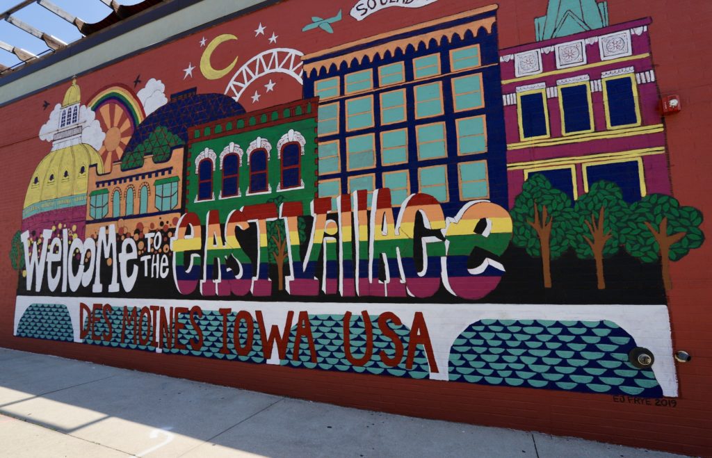 Colorful mural featuring painting buildings and trees, saying welcome to the east village Des Moines Iowa USA
