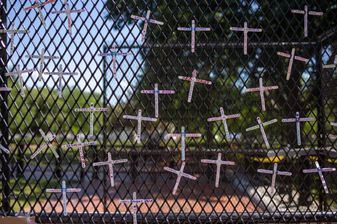 White crosses fashioned from popsicle sticks bear the names of Black lives lost too soon to police violence. Simple epitaphs include “brother,” “father,” “a friend,” and “loved music.”