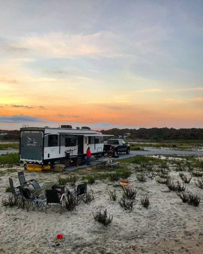 A sunset over an RV at a sandy campground