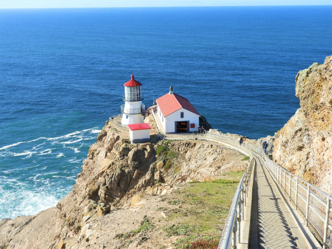 A view of the Point Reyes Lighthouse at the end of a long walkway and with the Pacific Ocean in the background.