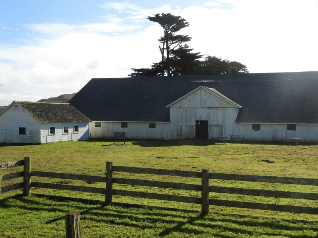 A historic barn with bright green grass and and old fence in the foreground.