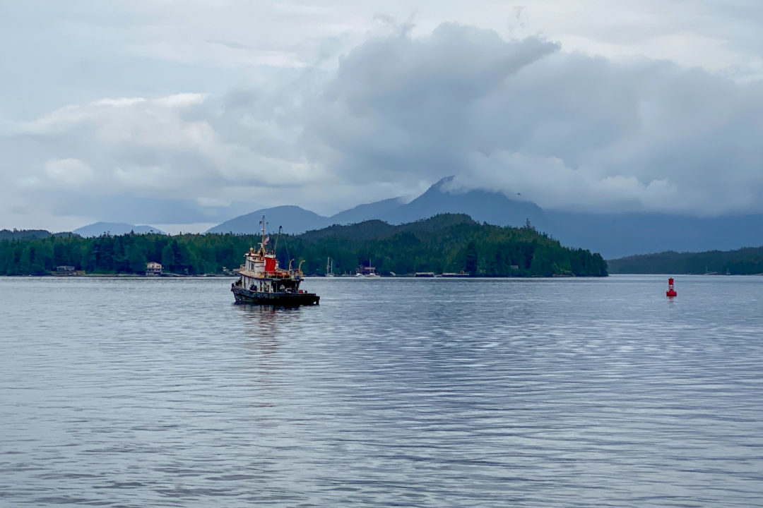 A lone fishing boat out on the water with a backdrop of mountains and an island
