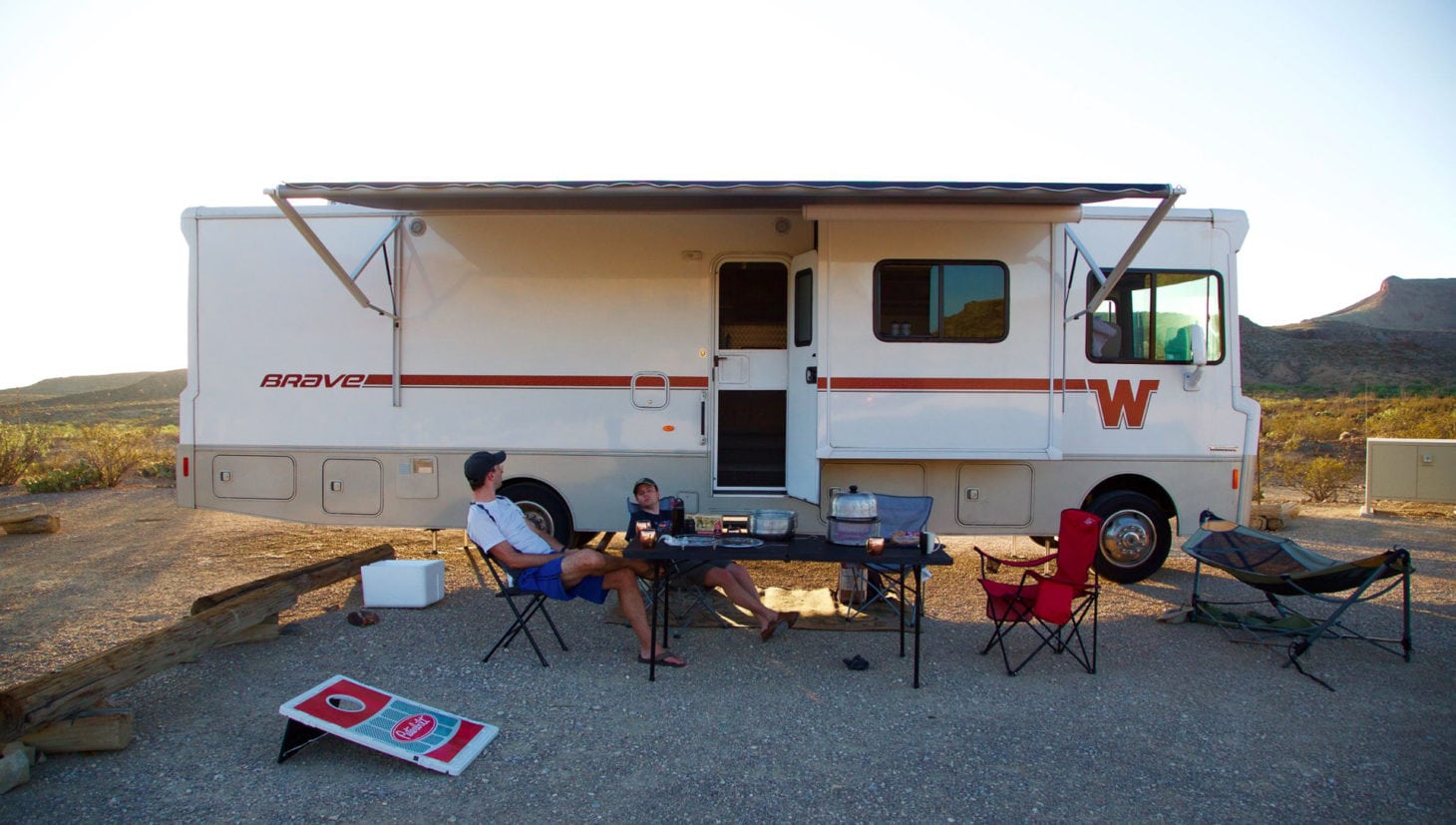 Two people outside rv while camping without hookups. Table and chair outdoor setup with games.