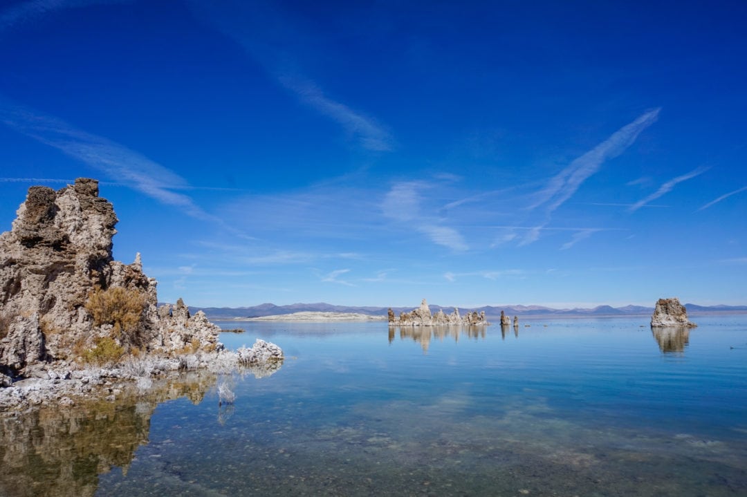 A blue lake against a blue sky, with rock spire formations rising up from the lake