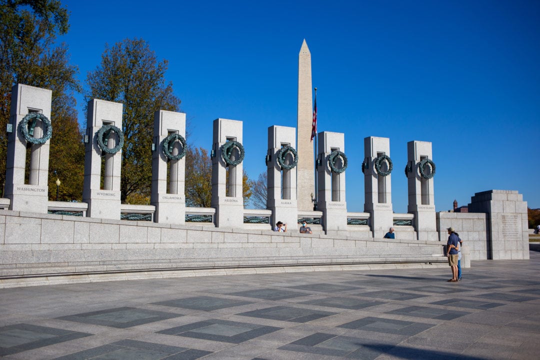 The World War II Memorial features a ring of granite columns each representing a U.S. state or territory. The memorial sits on the National Mall with views of the Washington Monument, the Lincoln Memorial, and the Capitol.