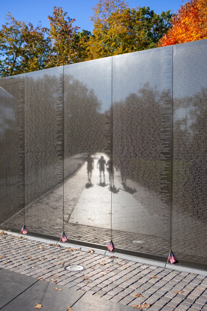 The shiny surface of the Vietnam Veterans Memorial wall is etched with names of the dead and missing but reflects back scenes of life from the National Mall.