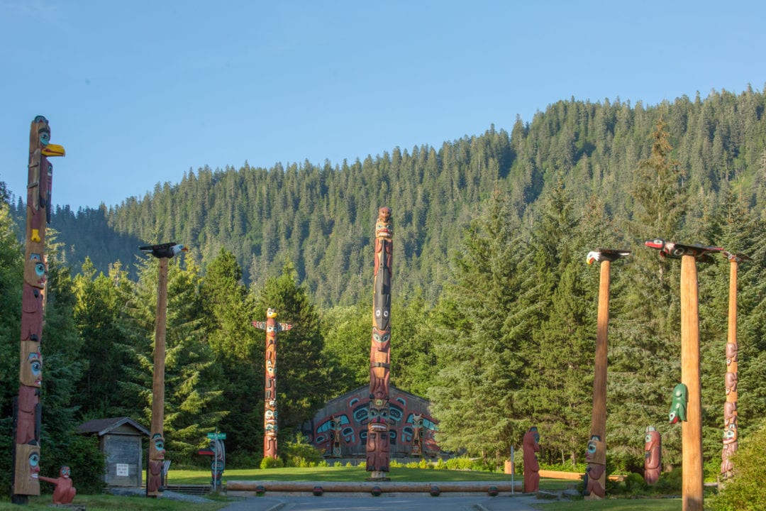 Several colorful totem poles surrounded by lush green pine forest.