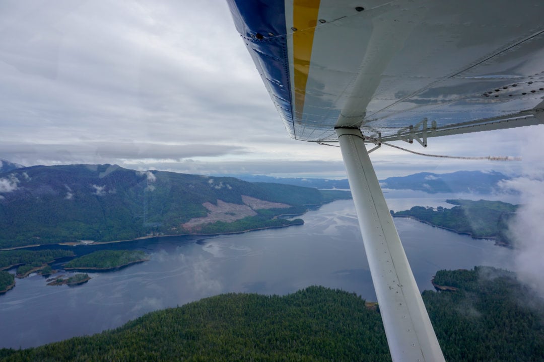 The view from beneath the wing of a float plane, looking out over water and green hills.