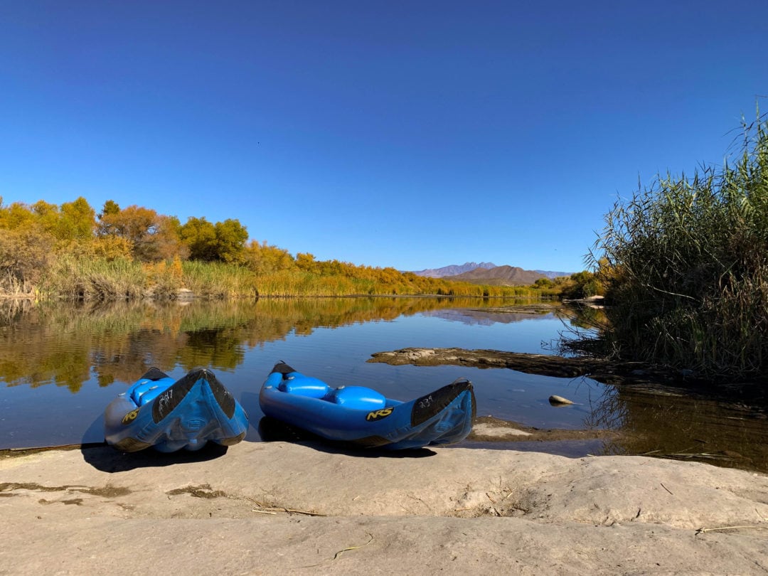 Two blue kayaks beached on rocky shore with view of the river in the background