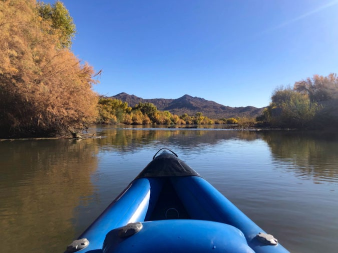 Front-facing view from kayak looking down river to yellow trees and mountains in the distance