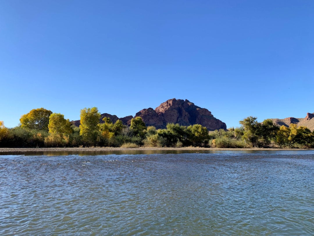 Red rock mountain in the background with green trees along wide river